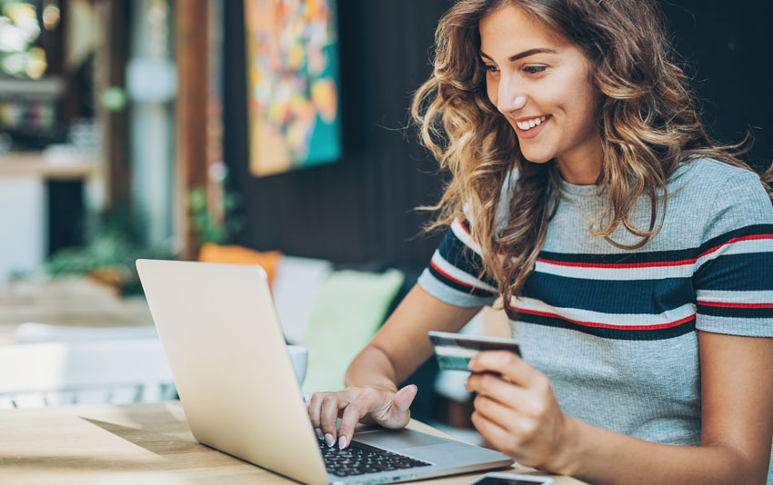 smiling female employee looking at laptop screen with a card in her hand